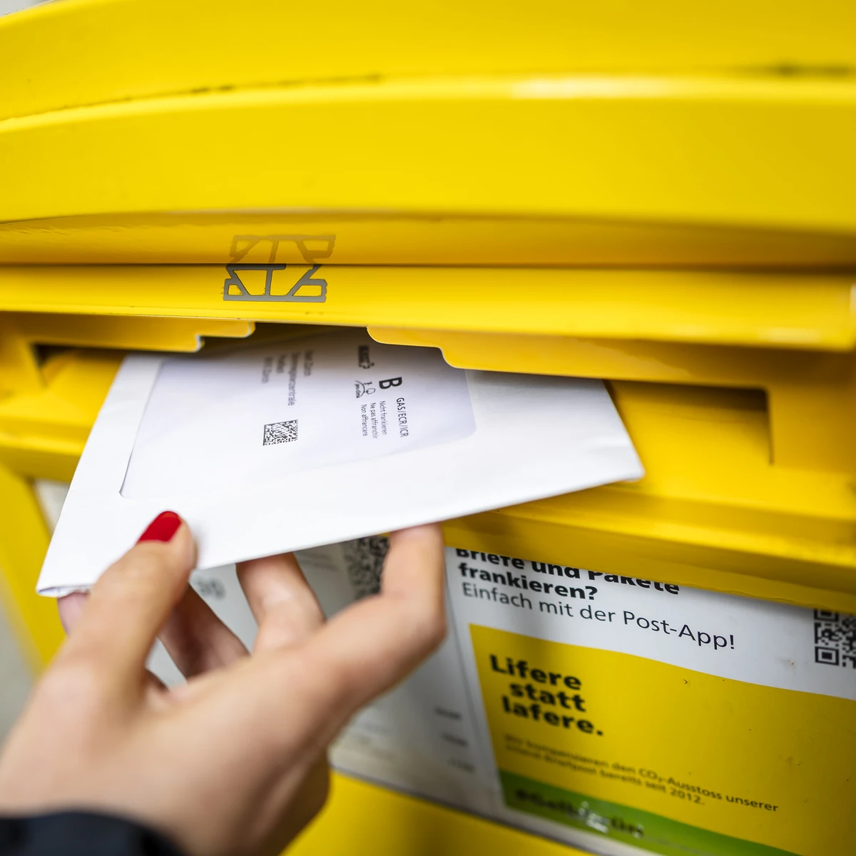 Brief wird in einen gelben Briefkasten der Schweizerischen Post eingeworfen
